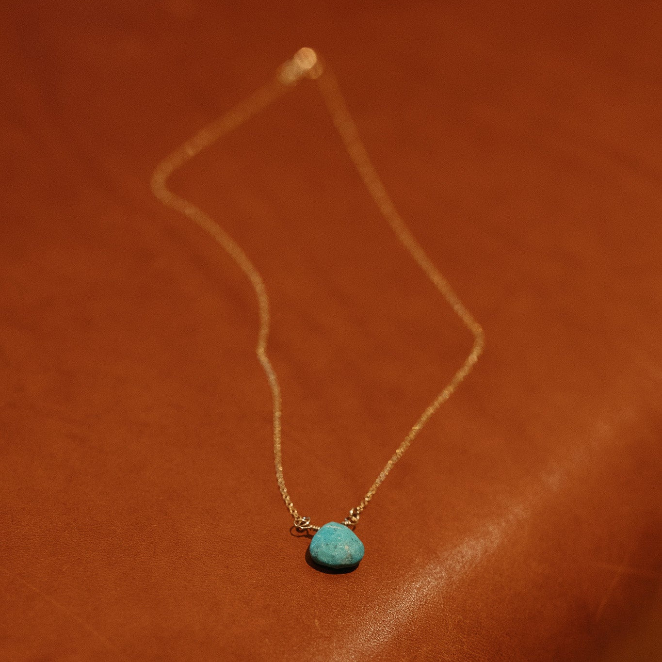 Turquoise Briolette Necklace with a gold chain on brown leather.