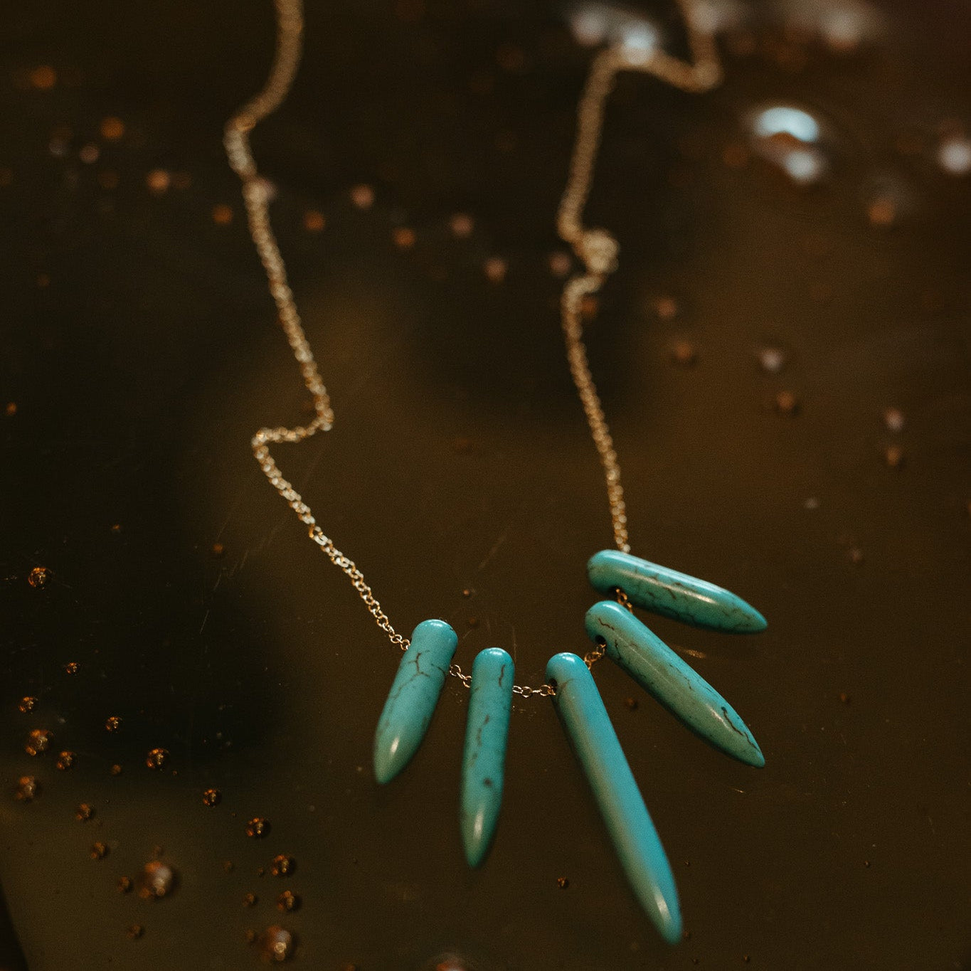 Turquoise howlite Spike necklace with a gold filled chain on a dark textured background. 