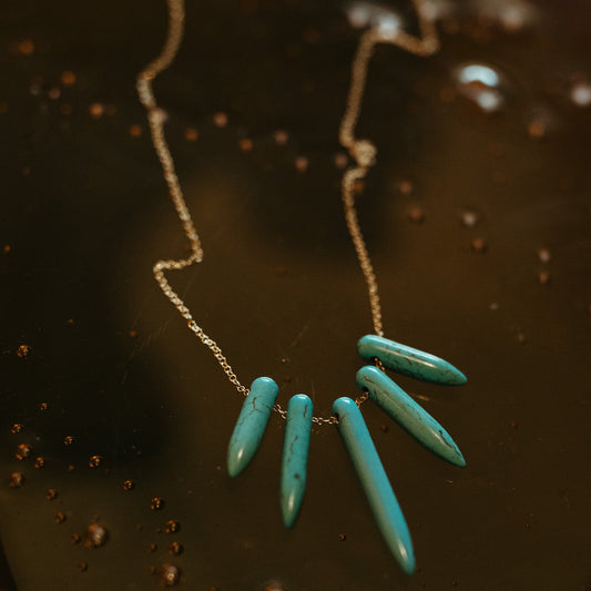 Turquoise howlite Spike necklace with a gold filled chain on a dark textured background. 