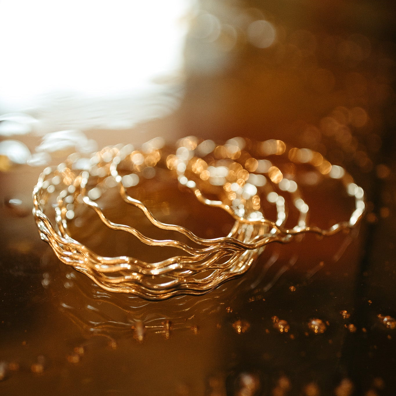 Close-up of a gold bracelet on a reflective surface with a blurred background