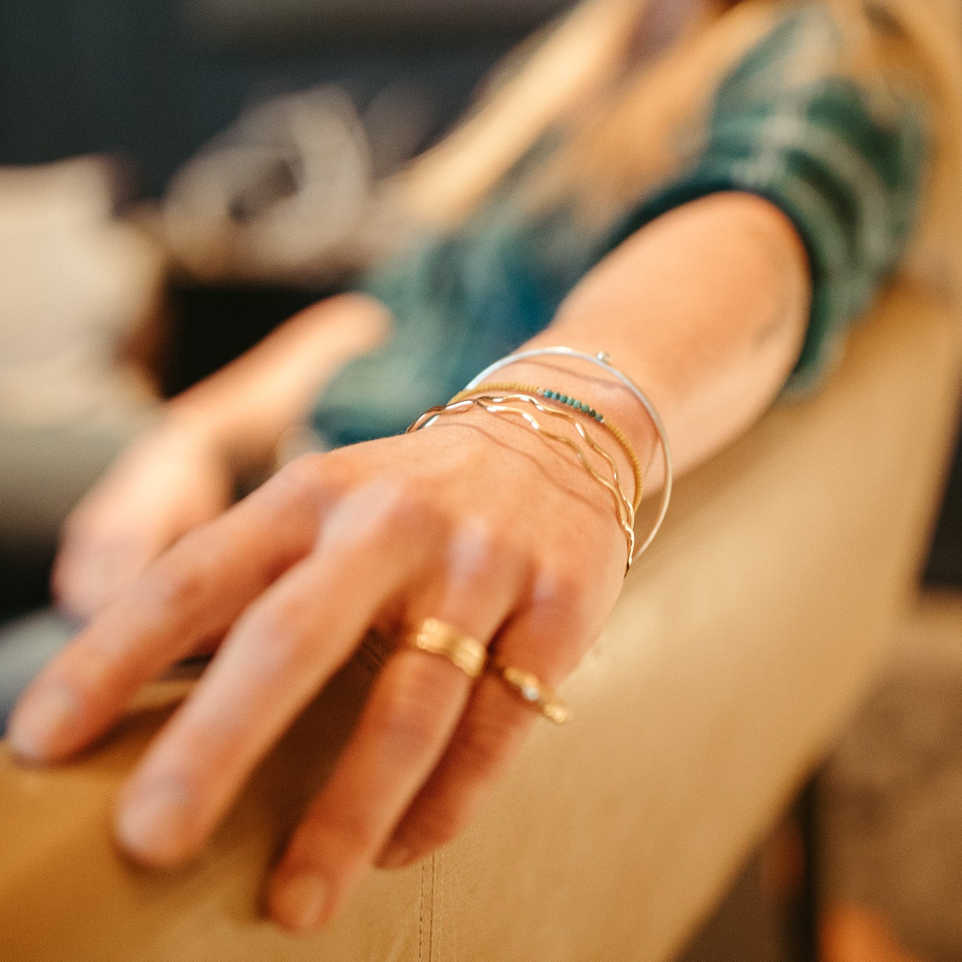 Close-up of a person's hand with multiple gold rings and bracelets on a blurred background