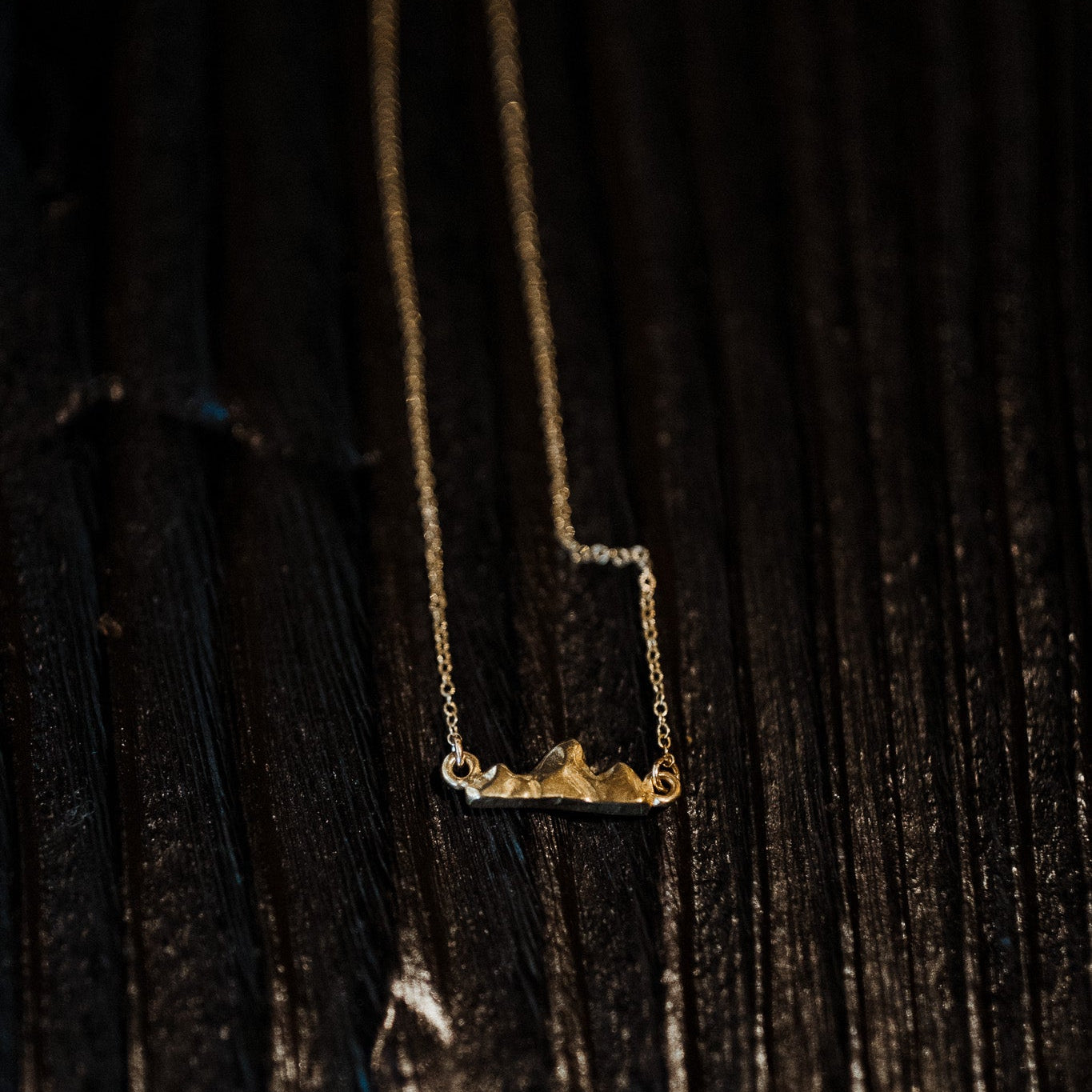 Close-up of delicate Teton III pendant showing miniature mountain detail on a black wood surface