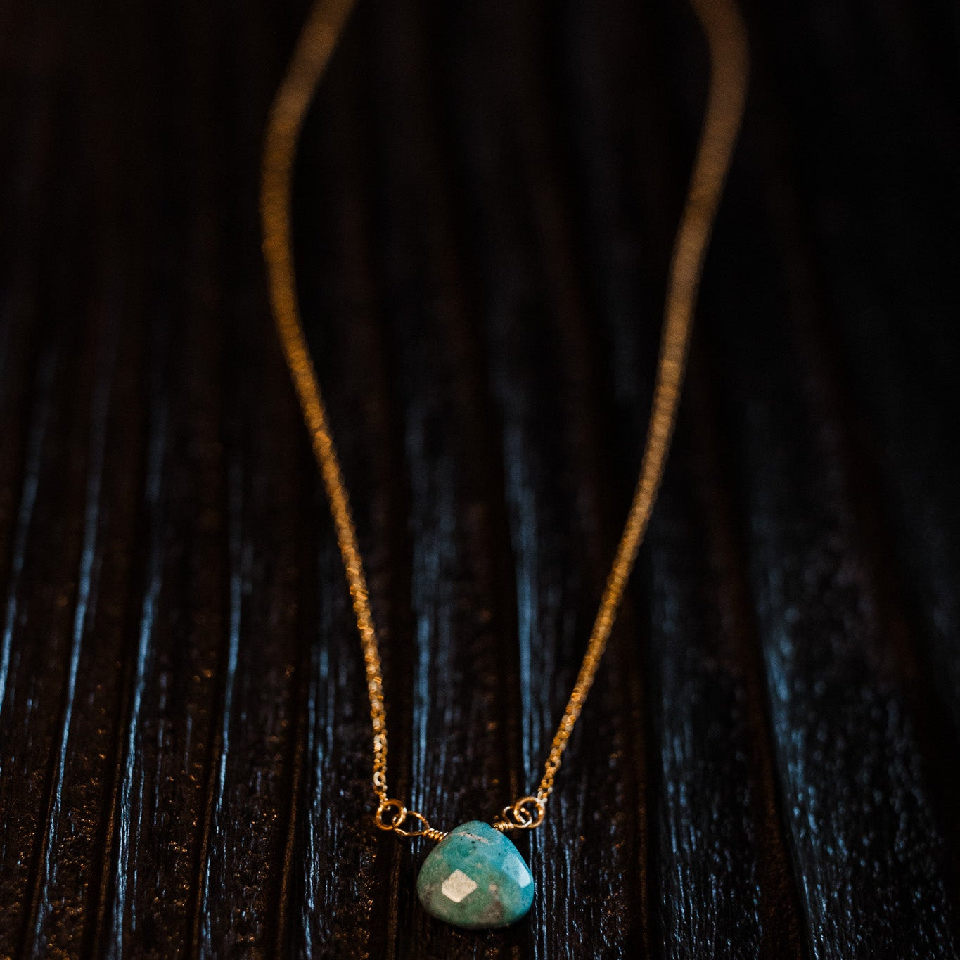 Turquoise Briolette Necklace with gold filled chain on a black wood background.