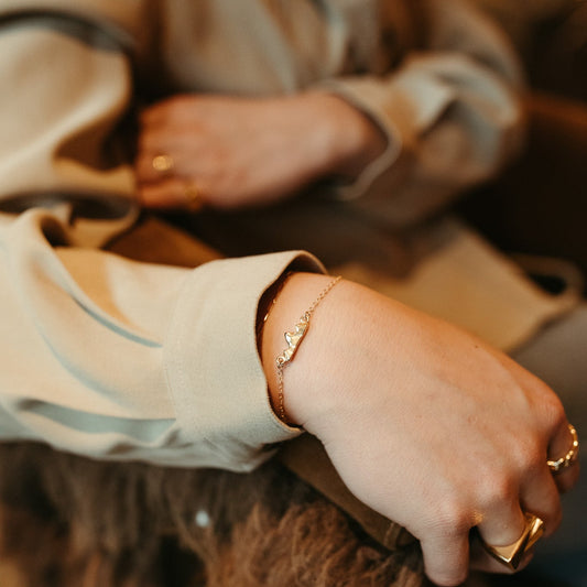 Close-up of a person's hand wearing a gold ring and bracelet, with a blurred background.