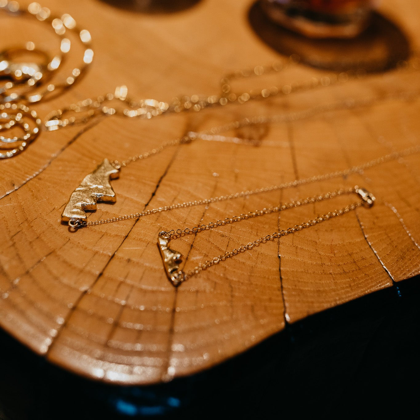 Close-up of Teton pendant charm on gold-filled chain bracelet on wood surface