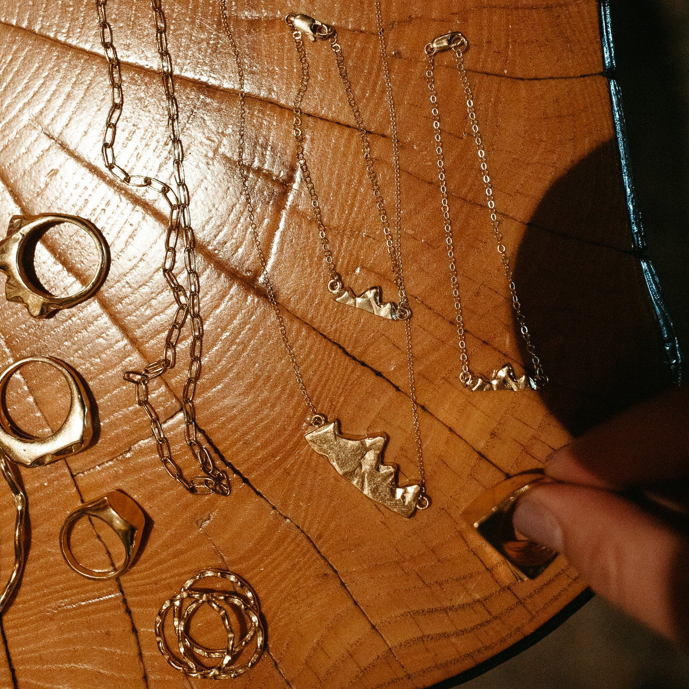 Close-up of Teton I, II, and III pendants and the Teton ring showing refined mountain silhouette on a wooden surface