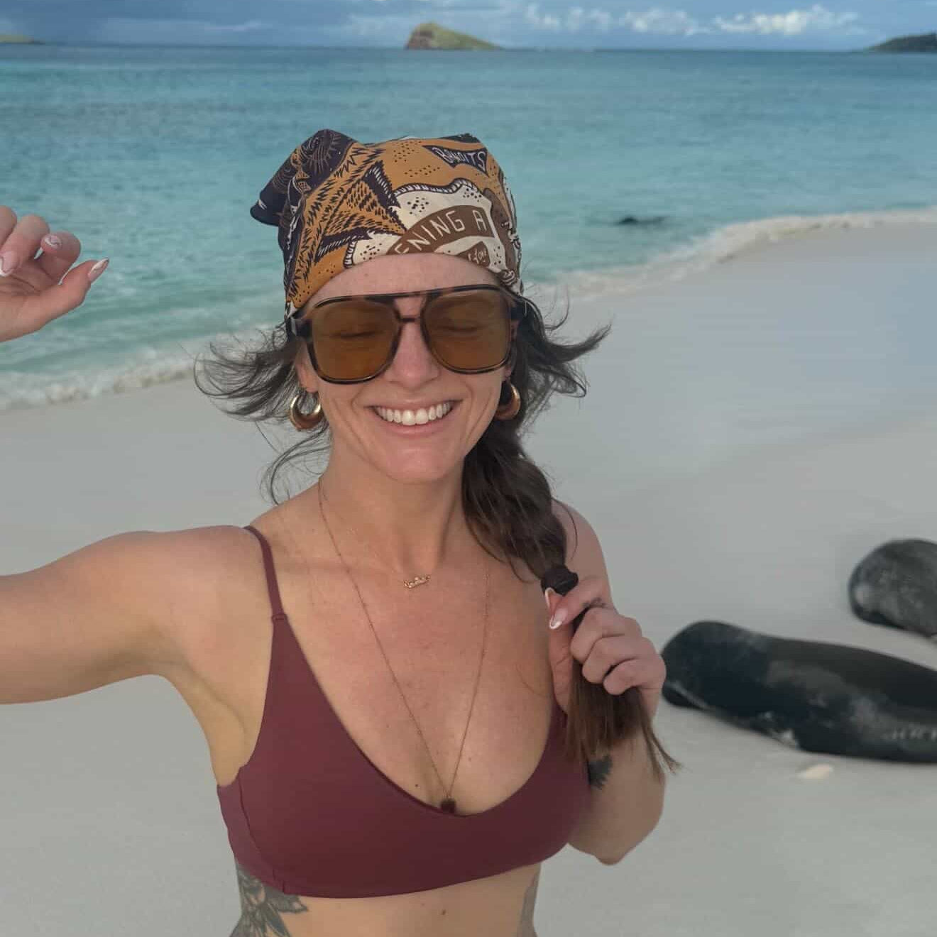 Woman wearing the small gold teton necklace on a beach in a bikini