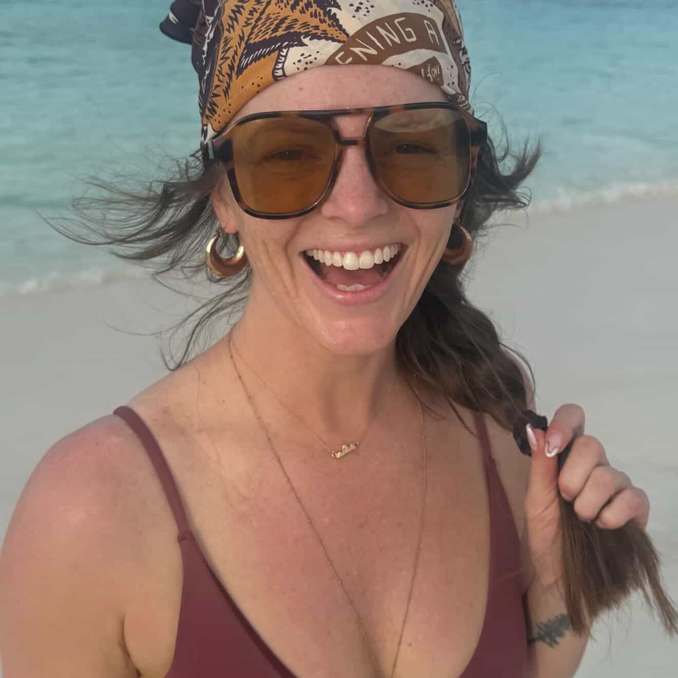 Woman wearing the small gold teton necklace on a beach in a bikini