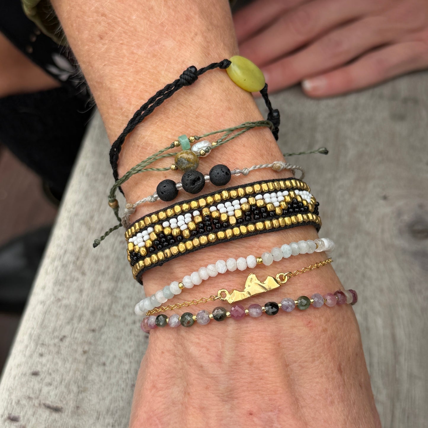 Close-up of a wrist wearing the gold vermeil Teton Bracelet stacked with multiple other bracelets. 