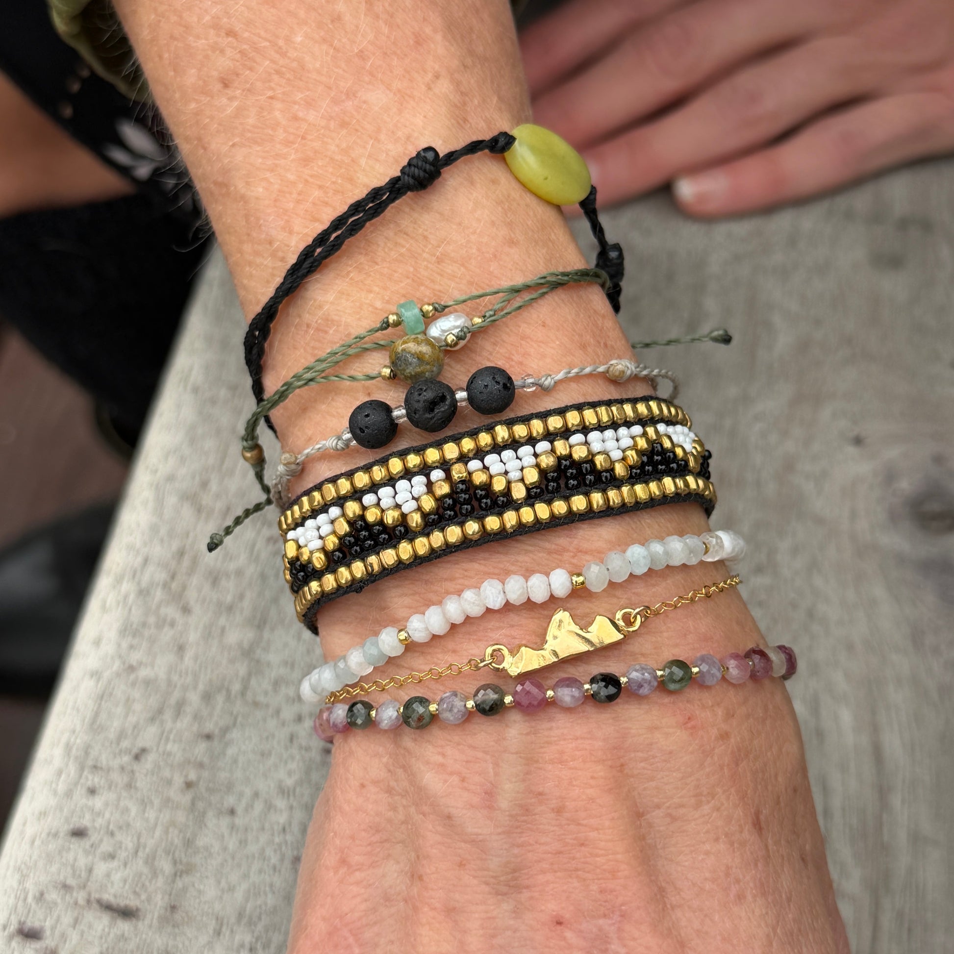 Close-up of a wrist wearing the gold vermeil Teton Bracelet stacked with multiple other bracelets. 