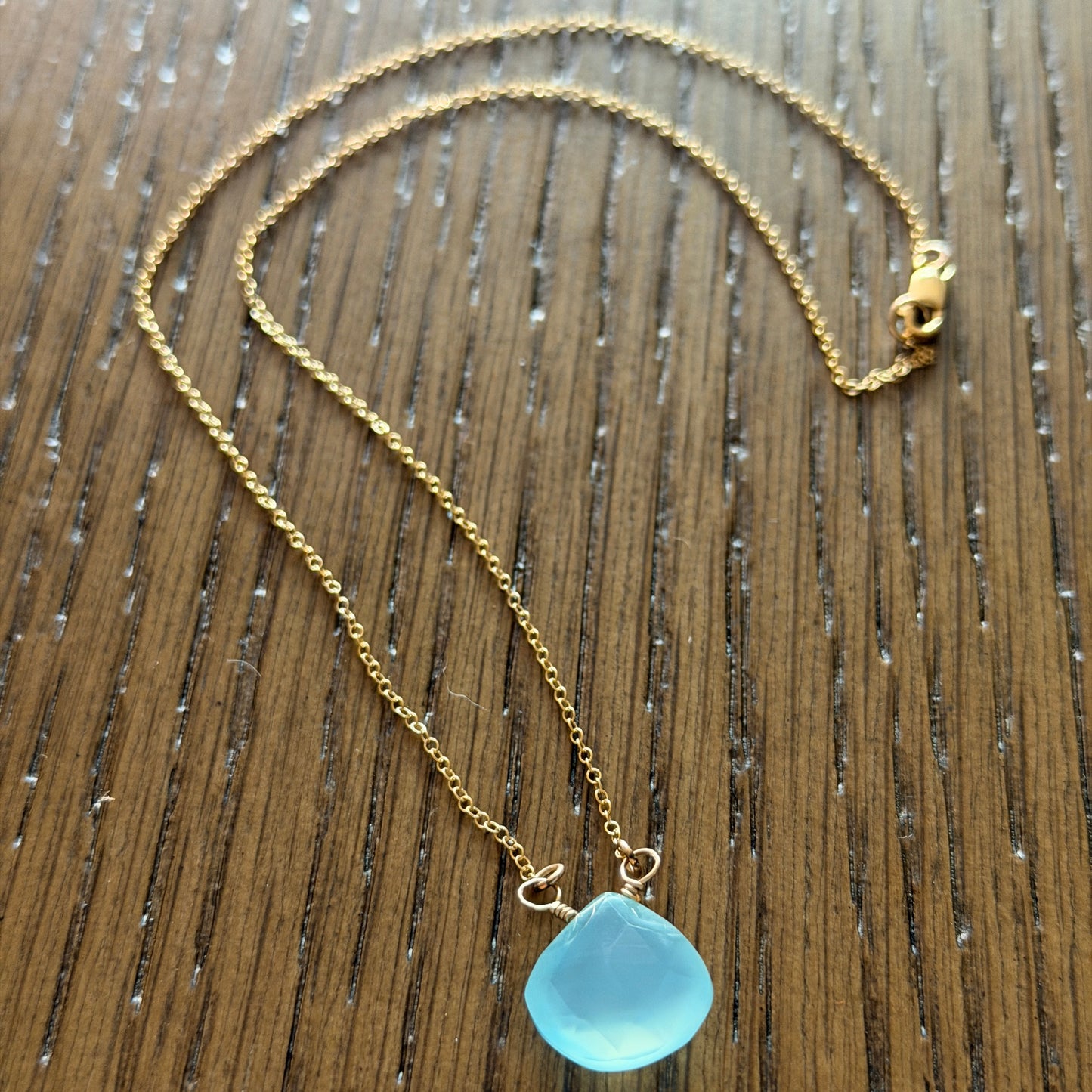 Close-up of faceted blue chalcedony briolette with gold-filled wire wrap showing translucent sea-glass finish