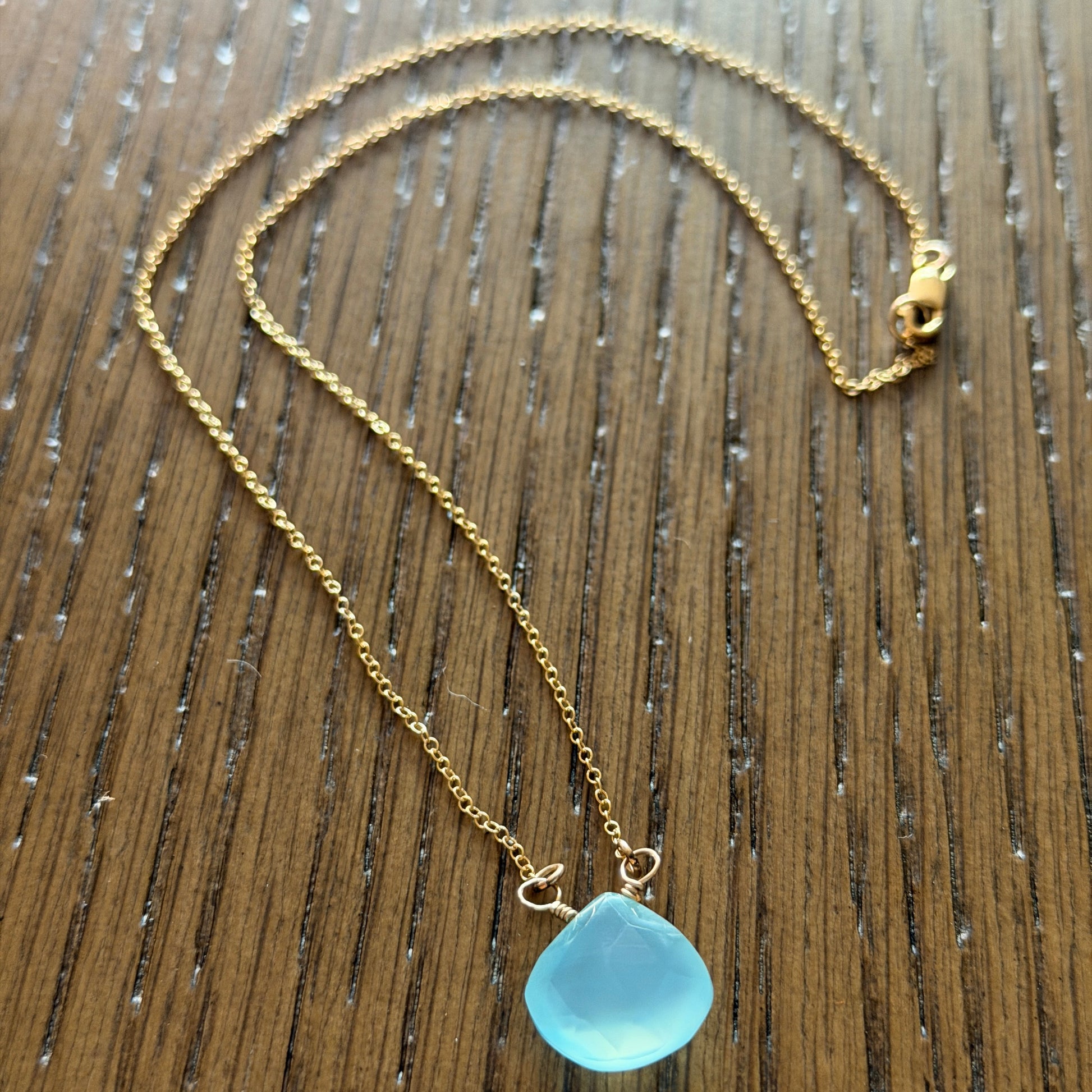 Close-up of faceted blue chalcedony briolette with gold-filled wire wrap showing translucent sea-glass finish