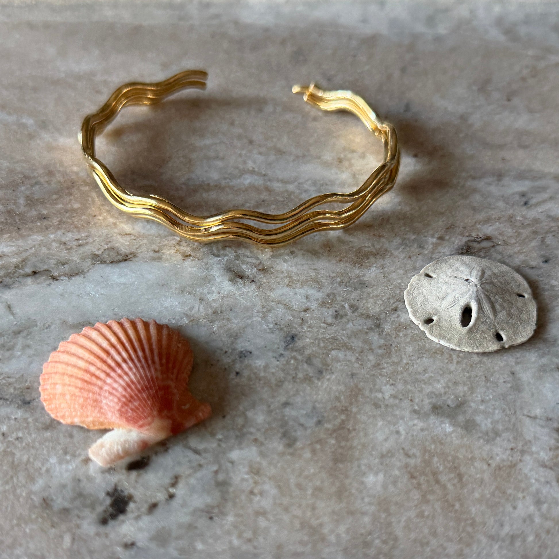 Gold vermeil wave bracelet and two shells on a marble surface