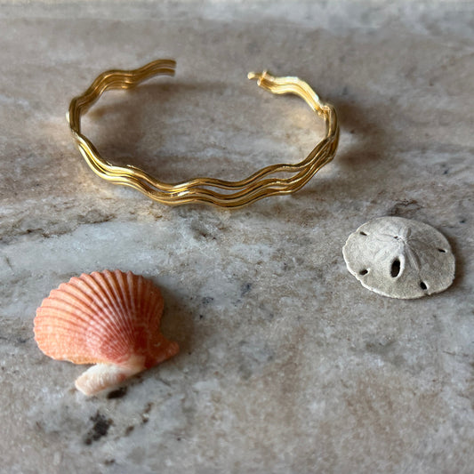 Gold vermeil wave bracelet and two shells on a marble surface