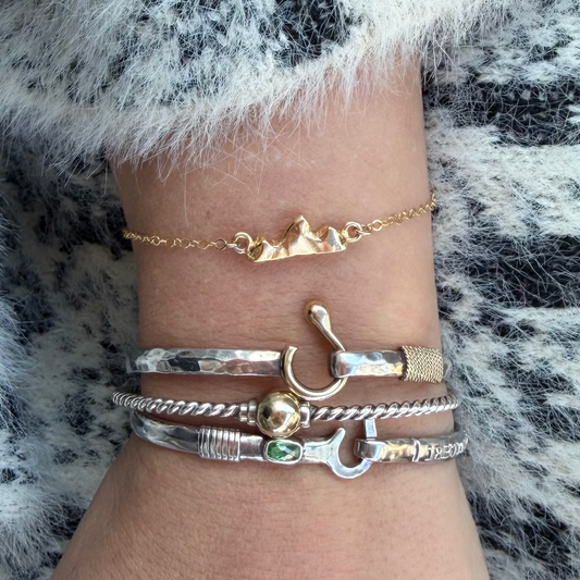 Close-up of a wrist wearing the gold vermeil Teton Bracelet and multiple gold and silver bracelets on a fur background
