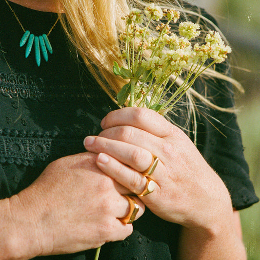 Woman wearing a turquoise and gold necklace holding flowers with gold rings on